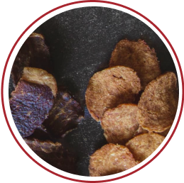 Two piles of different types of dried meat on a dark surface.